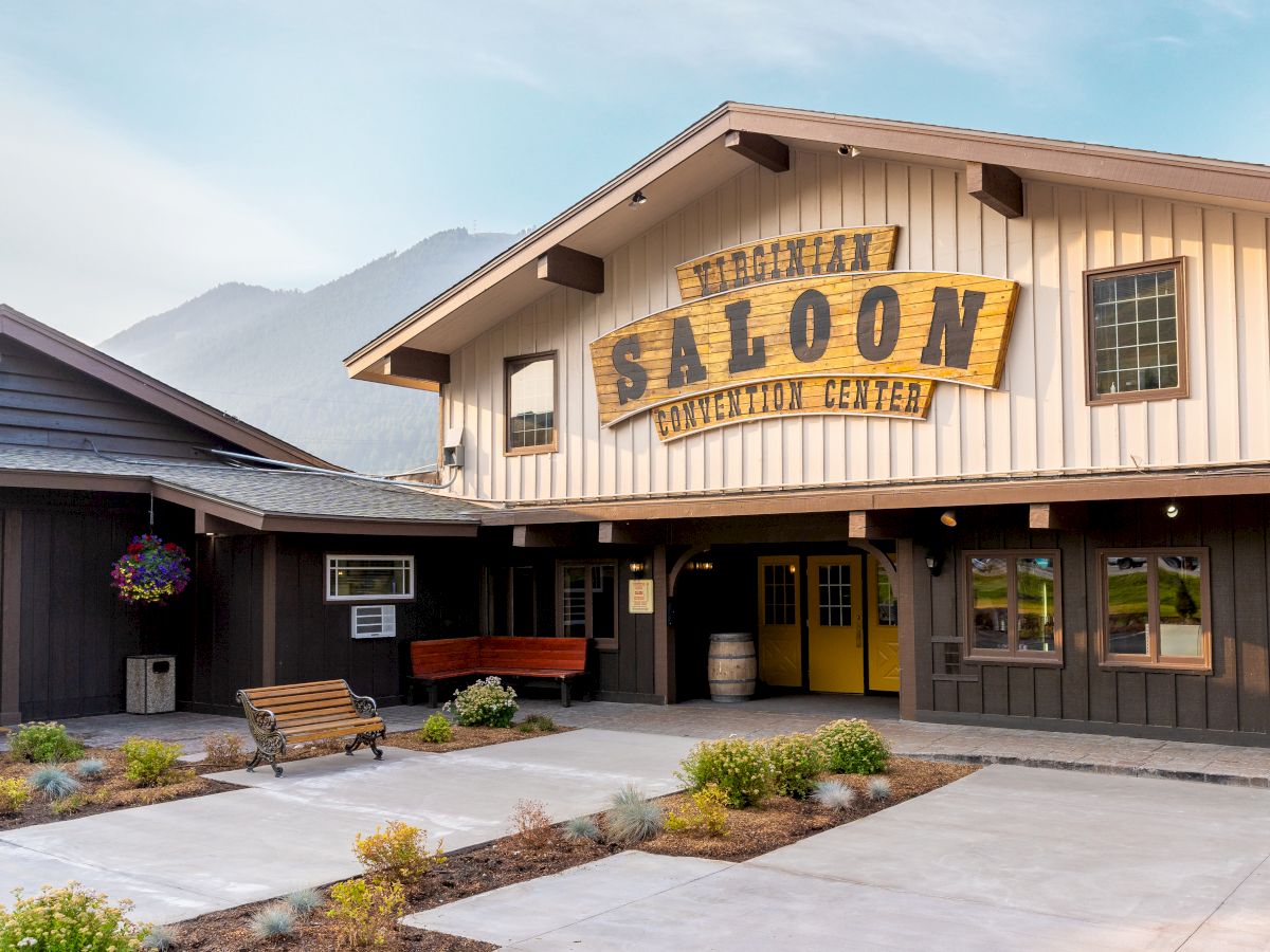 The image shows a rustic building labeled "Saloon Convention Center," with a wooden exterior, benches, and planters in the foreground.